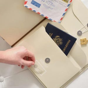 May include: A cream-coloured travel organiser folder featuring a magnetic snap closure, a pocket containing a dark blue United States passport, and an airmail envelope addressed to Merton College, Oxford, England, with a postage stamp.