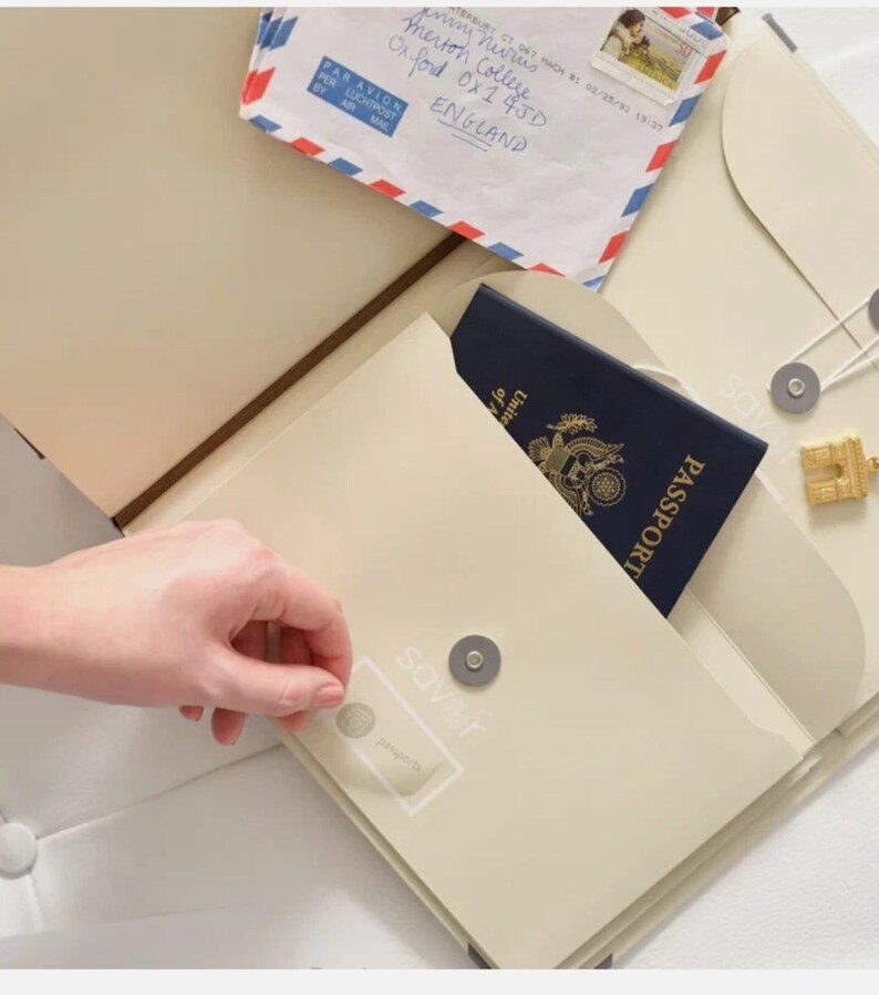 May include: A cream-coloured travel organiser folder featuring a magnetic snap closure, a pocket containing a dark blue United States passport, and an airmail envelope addressed to Merton College, Oxford, England, with a postage stamp.