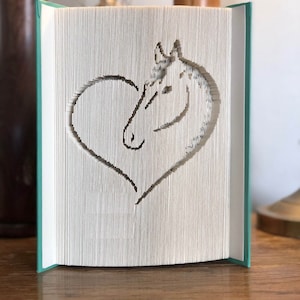 Peut inclure: Un livre turquoise avec une silhouette de tête de cheval blanche découpée dans les pages. La tête de cheval est à l'intérieur d'un cœur.