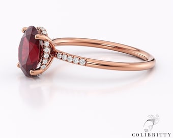 Può includere: Un anello di fidanzamento in oro rosa con una grande pietra preziosa rossa circondata da un alone di diamanti più piccoli. La fascia è anche incastonata con diamanti.