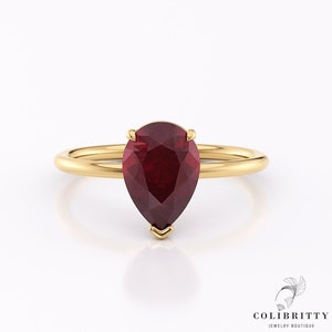Op de afbeelding: Een ring van goud met een peervormige robijn. De ring is simpel en elegant, met een gladde band en een delicate zetting voor de robijn.