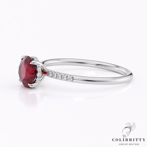 Può includere: Un anello d'argento con una pietra preziosa rossa e una fila di piccoli diamanti sulla fascia.