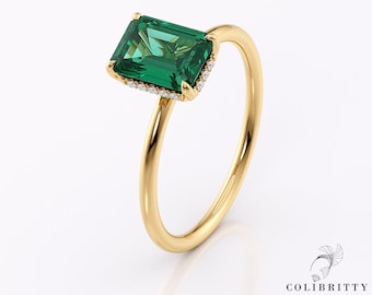 May include: A gold ring featuring a large, emerald-cut green gemstone. The gemstone is accented with small, clear stones around the edges. The ring has a simple, elegant band.