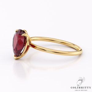 May include: A gold ring with a pear-shaped red gemstone set in a prong setting.