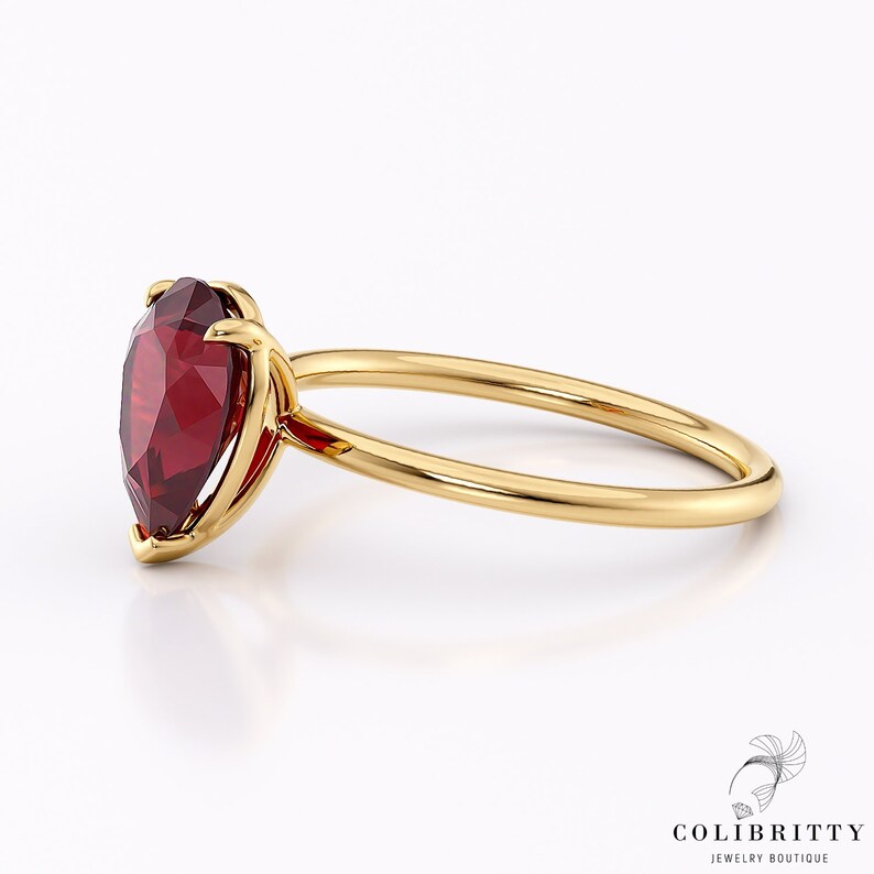 May include: A gold ring with a pear-shaped red gemstone set in a prong setting.