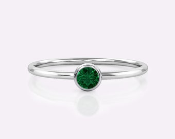 May include: A simple silver band ring with a bezel-set emerald green gemstone.