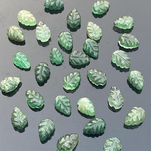 Può includere: Una collezione di ciondoli a forma di foglia in pietra preziosa verde. Le foglie sono intagliate con venature dettagliate e hanno un aspetto traslucido.