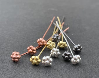 May include: A collection of metal headpins featuring small, textured flower-shaped ends. The pins are available in various metallic finishes, including copper, gold, silver, and dark gunmetal, each with a long, thin, straight wire stem.