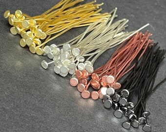 Può includere: Una collezione di chiodini a testa piatta in metallo disposti in quattro distinti gruppi di colore: oro, argento, oro rosa e nero. Ogni spillo presenta un sottile stelo in filo metallico sormontato da una piccola testa circolare piatta.