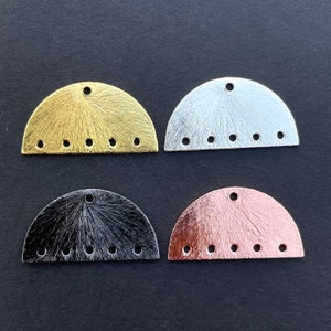 Pode incluir: Quatro pingentes de metal em forma de semicírculo em ouro, prata, preto e ouro rosa. Cada pingente tem uma superfície texturizada e seis furos igualmente espaçados ao longo da borda inferior.