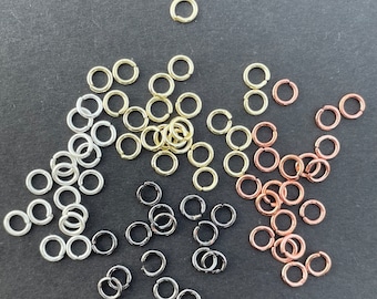 May include: A collection of small metal jump rings in various finishes including silver, gold, copper, and black. Each ring features a single cut opening, allowing them to be used as connectors for jewelry making and other craft projects.