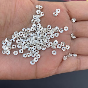 Peut inclure: Un grand tas de perles en métal argenté, chaque perle est un petit cercle plat avec un trou au centre.