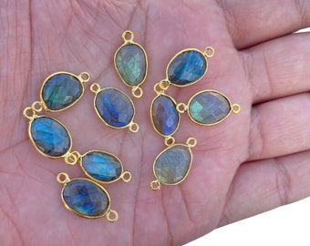 May include: A collection of eight oval-shaped labradorite gemstones, each set in a gold-toned metal bezel with two small loops on opposite ends. The stones exhibit iridescent flashes of blue, green, and grey with a faceted surface texture.