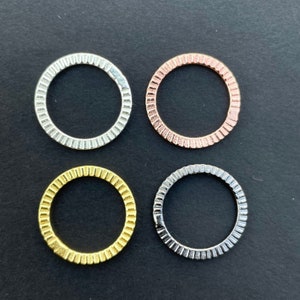 May include: Four metal rings with a decorative, ridged edge. The rings are silver, gold, rose gold, and a darker silver.