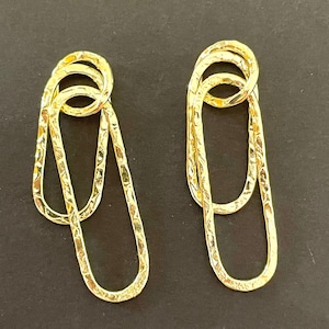 May include: A pair of gold-toned earrings with a textured finish. Each earring features two interlocking oval shapes.