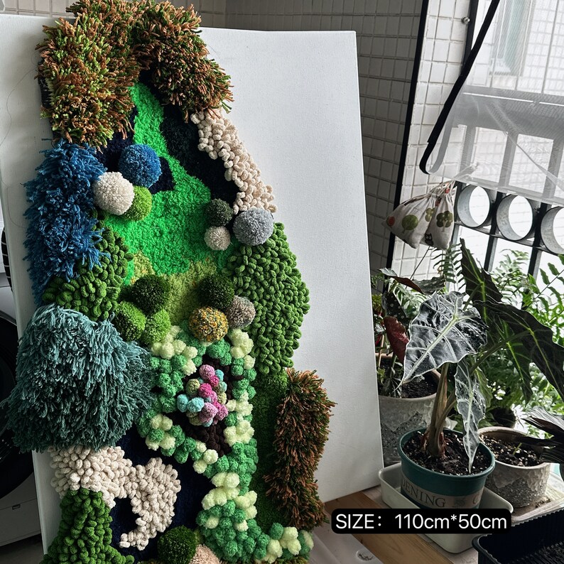 May include: A green, blue, and white yarn wall hanging with a textured, 3D design. The wall hanging is on a white canvas and has the text "SIZE: 110cm*50cm" at the bottom.