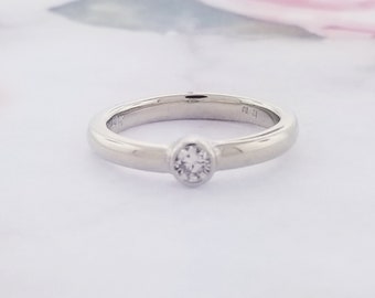 Puede incluir: Un anillo de banda simple de plata con un solo diamante redondo engastado en un engaste de bisel.