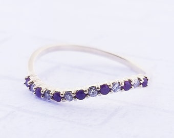May include: A gold band ring with a curved row of purple and white gemstones.