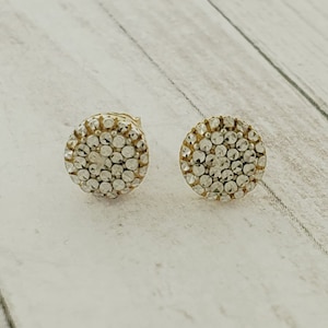 May include: A pair of gold stud earrings with a round design featuring small, clear stones.