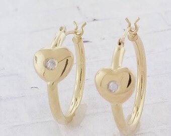May include: A pair of gold hoop earrings with a heart-shaped design and a small clear stone in the center of each heart.