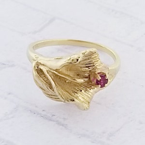 May include: A gold ring with a detailed floral design and a single red gemstone.