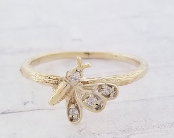 Op de afbeelding: Een gouden ring met een delicaat vlinderontwerp met kleine heldere diamanten. De band van de ring heeft een textuur.