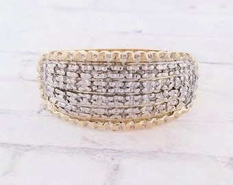May include: A gold band ring with a wide, pave-set diamond band. The ring has a textured, milgrain edge.