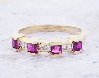 May include: A gold band ring with five square-shaped pink gemstones and smaller clear gemstones set in between.