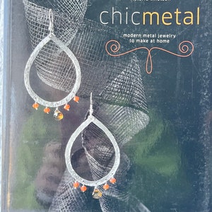 May include: A book titled "chicmetal" by Victoria Tillotson, featuring a close-up of silver earrings with orange gemstones. The book cover is black with a silver mesh pattern.