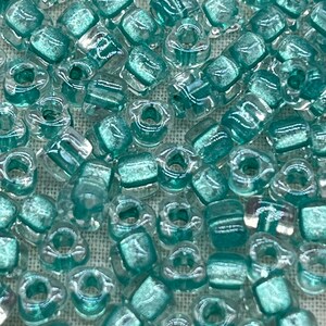 May include: A close-up of a pile of small, square, transparent beads with a light teal iridescent finish.