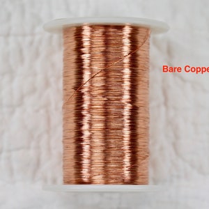 May include: A spool of bare copper wire, wound tightly on a white plastic spool. The wire is a warm copper color.