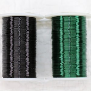 May include: Two spools of wire, one black and one green, are shown on a white surface. The wire is wound tightly around the spools.