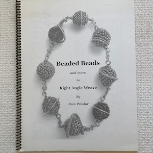 May include: A black and white photo of a book titled "Beaded Beads and more in Right Angle Weave by Pam Preslar". The book cover features a silver beaded necklace with a close-up of the beads.