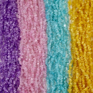 May include: Four strands of gemstone chips in various colors. The strands are purple, pink, light blue, and yellow. The chips are small and irregular in shape.