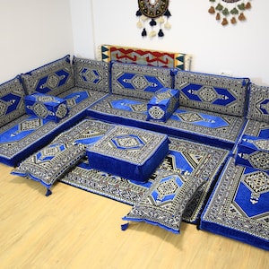 Puede incluir: Un conjunto de asientos de suelo azul y blanco con varios cojines y una alfombra grande. El conjunto está dispuesto en forma de U e incluye cojines de diferentes tamaños y formas.
