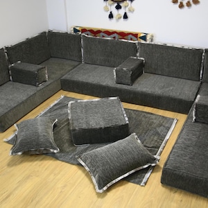 Könnte beinhalten: Ein graues L-förmiges Ecksofa mit mehreren Kissen und Polstern. Das Sofa ist aus einem weichen, strukturierten Stoff gefertigt und hat ein modernes Design.