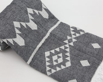 Peut inclure: Une serviette turque à franges avec un motif gris et blanc. La serviette présente un motif géométrique avec des triangles et des diamants blancs sur un fond gris.