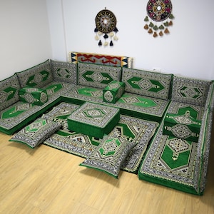 Puede incluir: Un conjunto de asientos de suelo con estampado verde y dorado con un puf cuadrado. El conjunto incluye varios cojines y almohadas, todos con diseños intrincados.