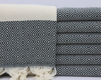 May include: A white and black patterned Turkish towel with fringe. The towel is folded and stacked, showing the pattern.