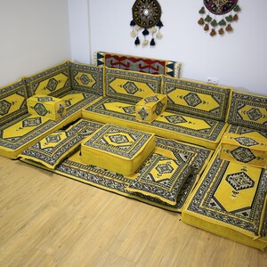 Puede incluir: Un conjunto de asientos de suelo con estampado amarillo y negro con múltiples cojines y un puf cuadrado. El conjunto está dispuesto en forma de U y es perfecto para relajarse y entretener.