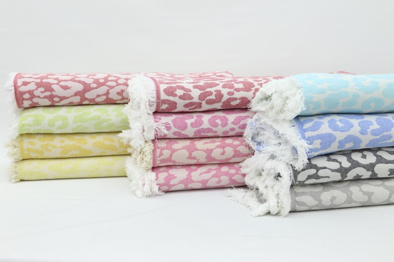 May include: A stack of six colorful towels with a leopard print design. The towels are folded and have a white fringe around the edges.