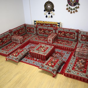 Può includere: Un set di sedute a pavimento rosso e nero con motivi, con più cuscini e cuscini. Il set è disposto a forma di U e include cuscini di diverse dimensioni e forme.