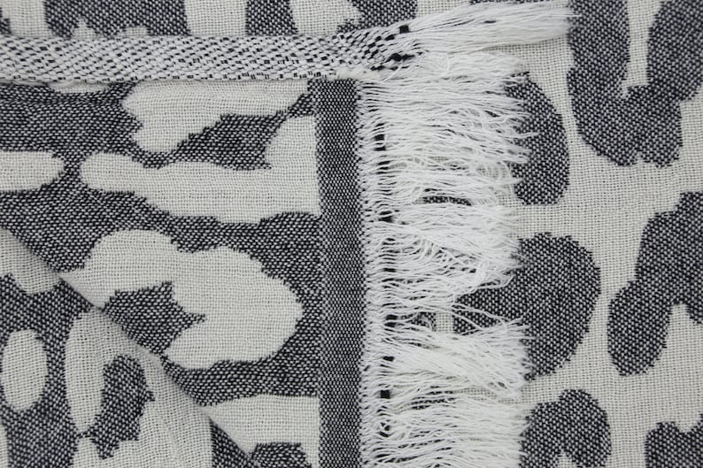 May include: A white and black throw blanket with a leopard print pattern. The blanket has a fringe border and is made of a soft, woven fabric.