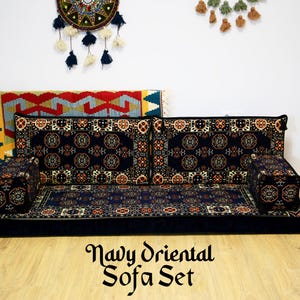 May include: Navy blue floor sofa set with a traditional oriental patterned design. The set includes a large sofa cushion, two smaller cushions, and two armrests. The sofa set is on a wooden floor.