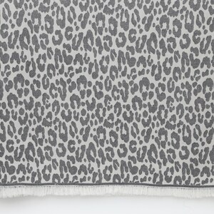 May include: A gray and white throw blanket with a leopard print pattern. The blanket has a fringe border.