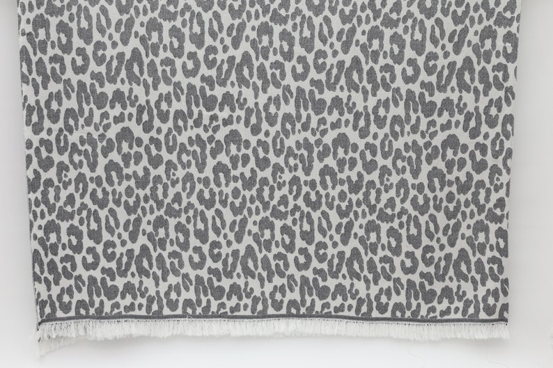 May include: A gray and white throw blanket with a leopard print pattern. The blanket has a fringe border.