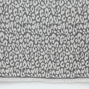 May include: A gray and white patterned throw blanket with a fringe border. The pattern is a repeating leopard print.
