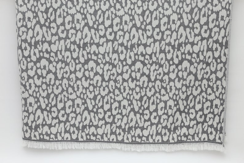 May include: A gray and white patterned throw blanket with a fringe border. The pattern is a repeating leopard print.