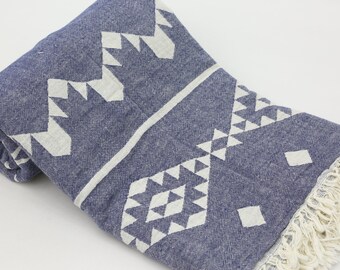 May include: A folded blue and white patterned textile with a geometric design. The textile features a repeating pattern of white triangles and diamonds on a blue background. The edge has a fringe.