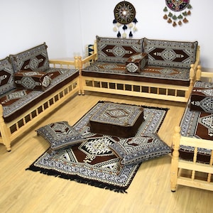 May include: A traditional Moroccan seating set with a brown and white patterned fabric. The set includes a sofa, two chairs, a coffee table, and several throw pillows. The furniture is made of light wood and has a simple, elegant design.